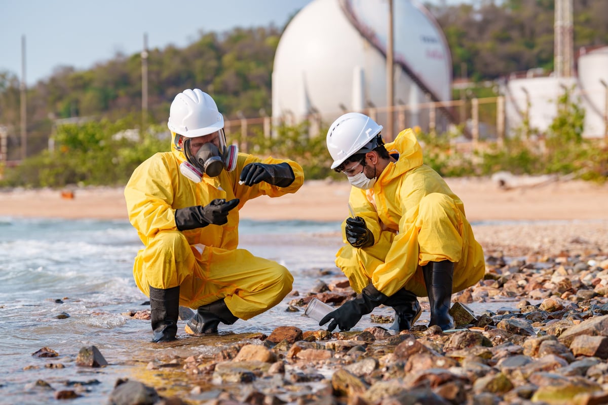 Workers in protective suits collecting samples on a shoreline